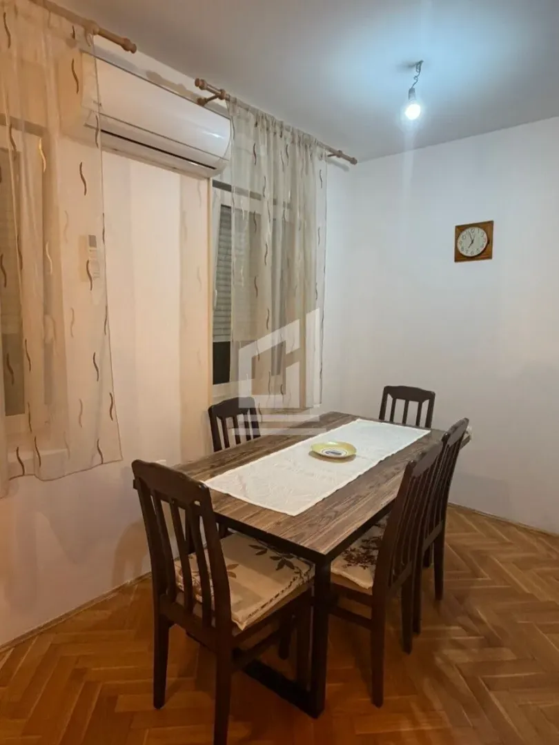 Dining area with a wooden table and chairs, parquet flooring, and curtained windows.