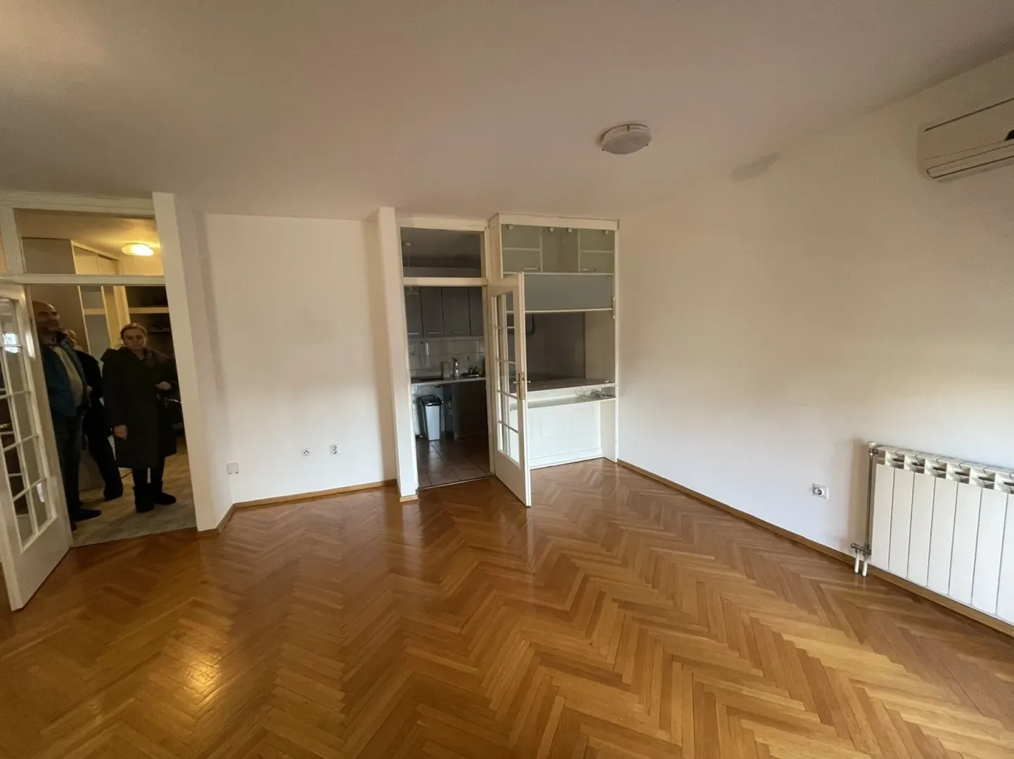 Empty room with parquet flooring and an entrance to the kitchen.