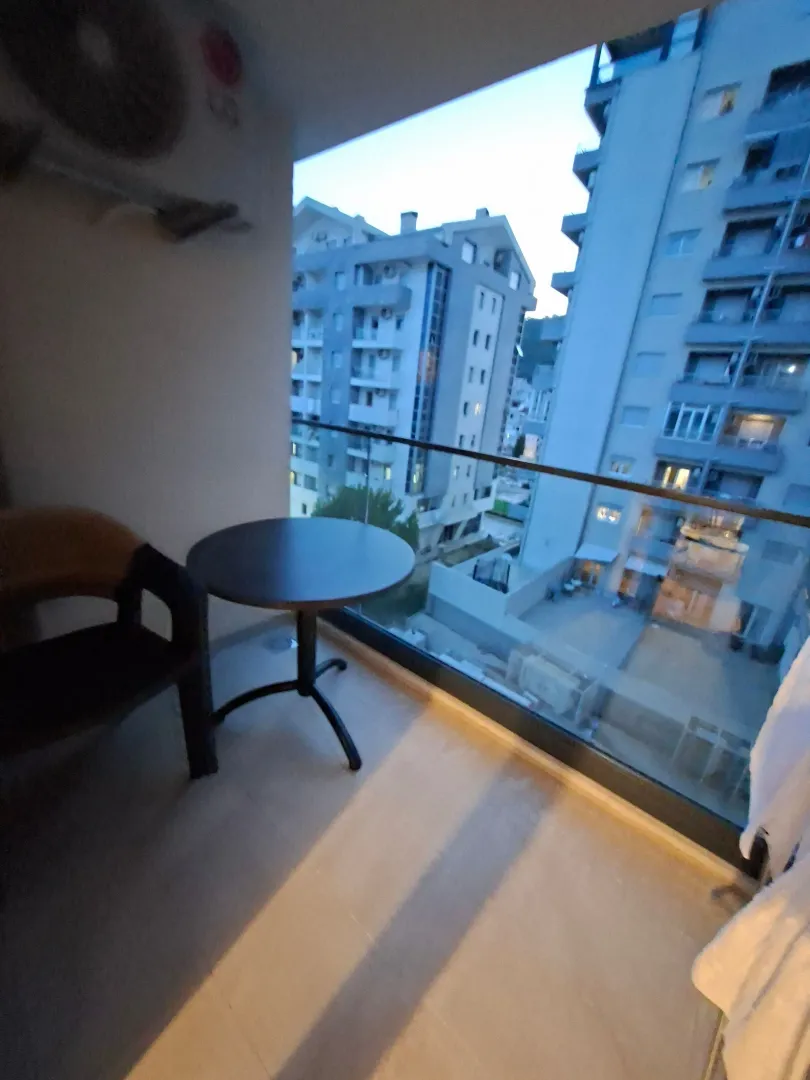 Furnished balcony with a small table and chair, overlooking surrounding buildings.