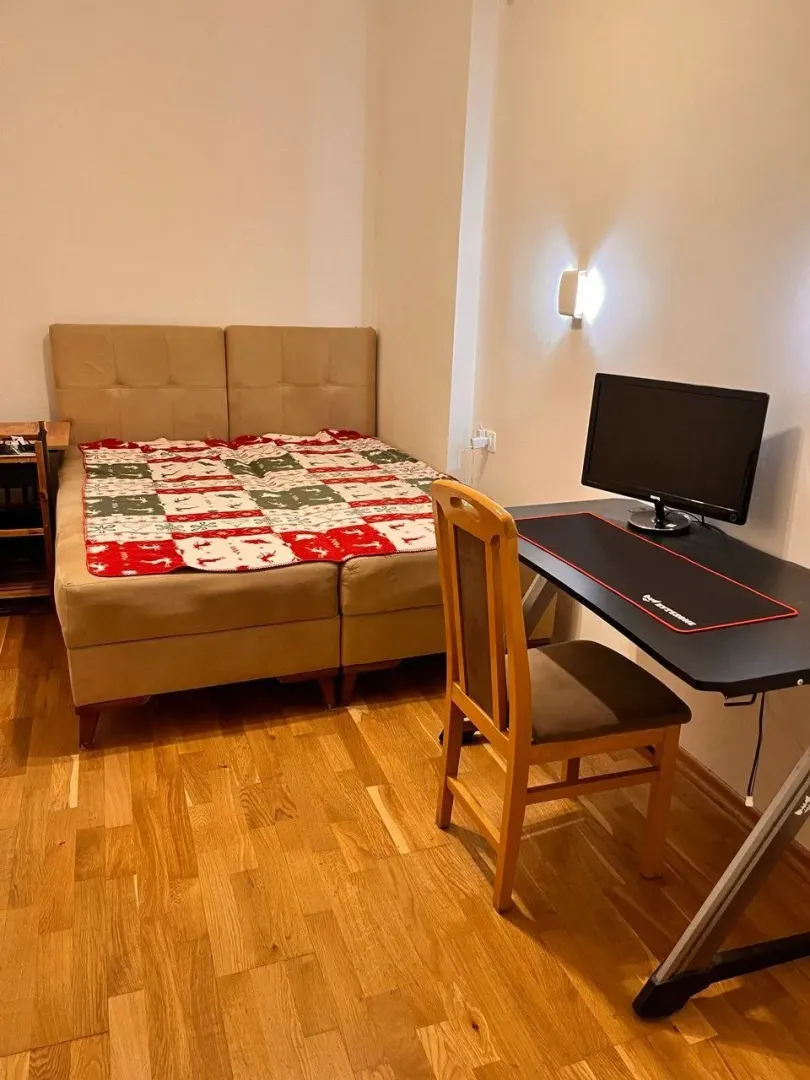 Spavaća soba sa bračnim krevetom i radnim stolom sa računarom.