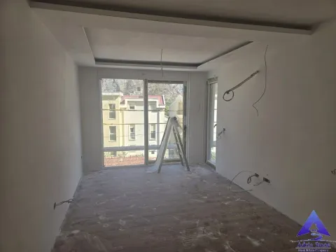 Nenameštena prostorija u sivoj fazi sa balkonskim vratima i pogledom na naselje. - image 18