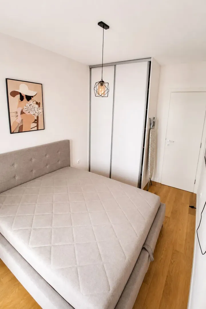 Bright bedroom with a double bed, white wardrobe, and wooden flooring.