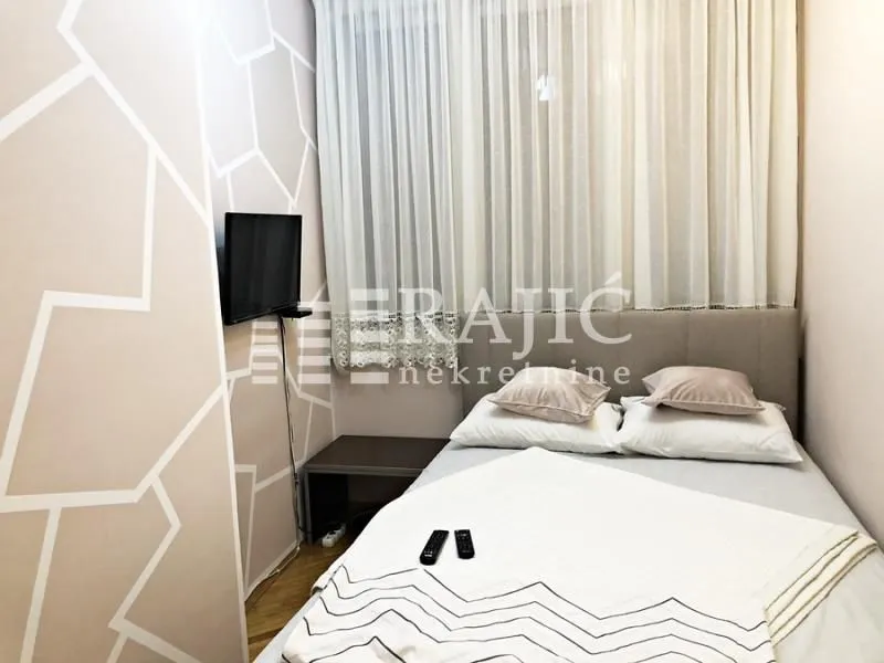 Smaller bedroom with a double bed, wall-mounted TV, and window with curtains.