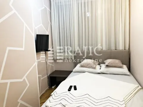 Smaller bedroom with a double bed, wall-mounted TV, and window with curtains. - image 4