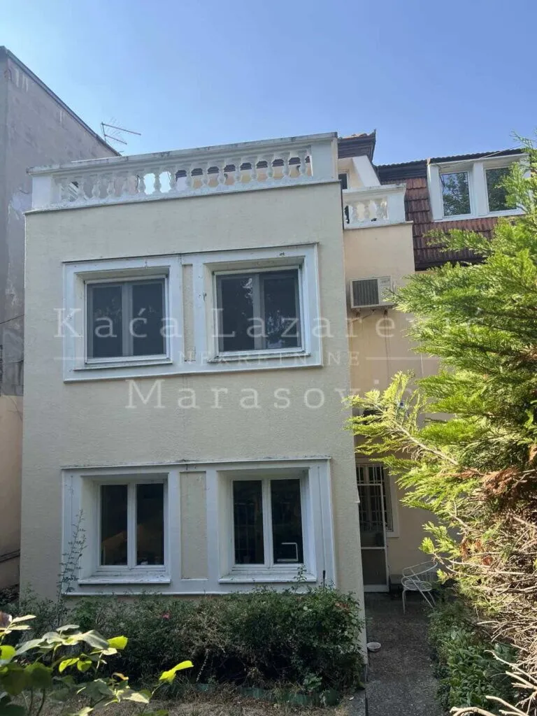 Pogled na spoljašnjost zgrade sa terasom i zelenilom u dvorištu.