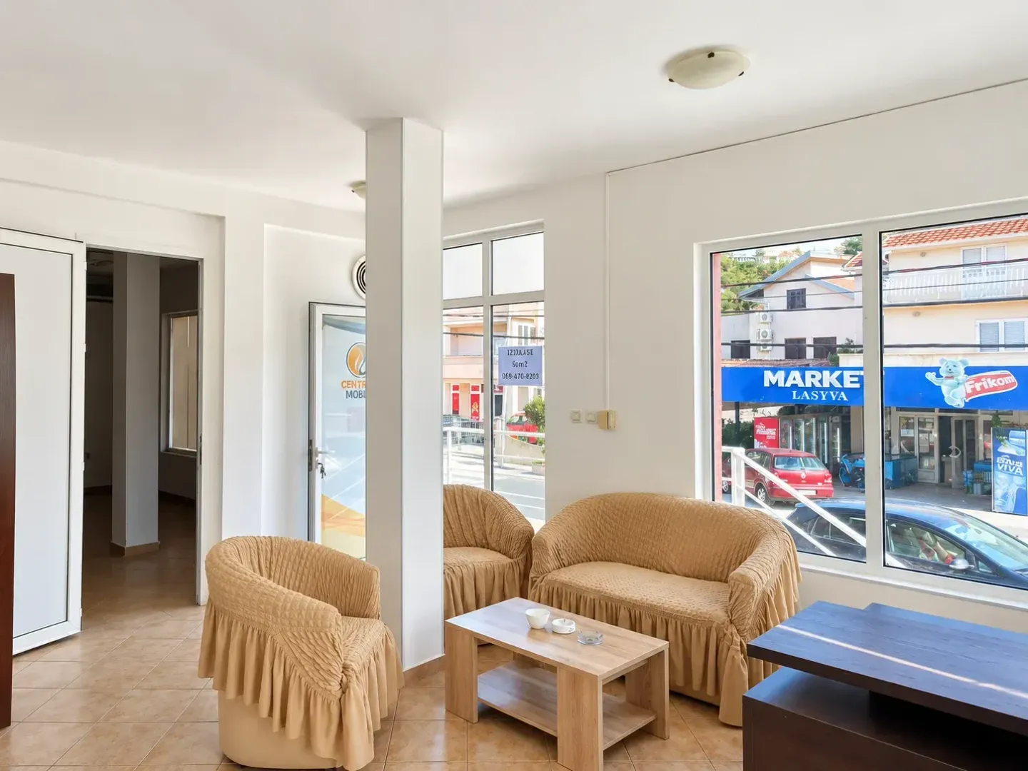 Bright living room with seating furniture and large windows overlooking the street.