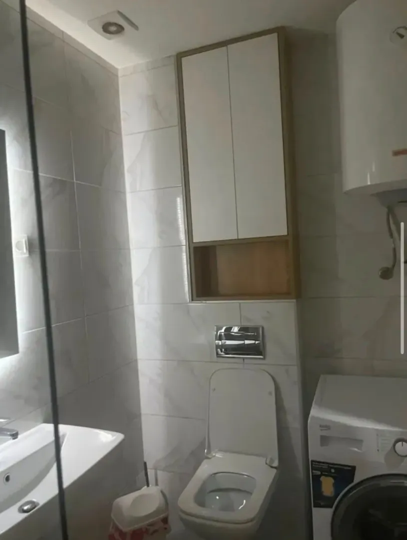 Pogled na moderno opremljeno kupatilo sa wc šoljom, umivaonikom i veš mašinom.