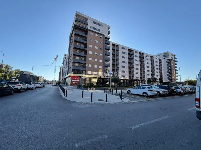 Pogled na spoljašnjost moderne stambene zgrade sa parkingom i ulicom u prvom planu.